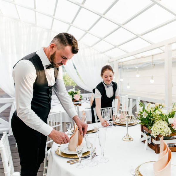 Two male and female waiters serve a table in the restaurant wiping glasses for wine